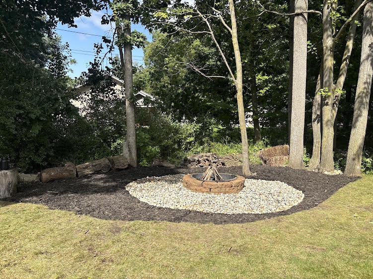 Backyard fire pit surrounded by river rock and mulch